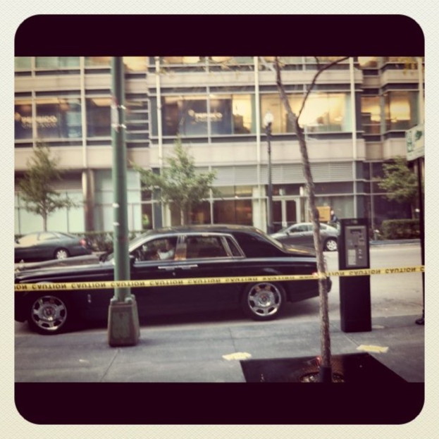 Ein Auto ist in der Mitte des Bildes zu sehen, umgeben von Pfählen und Bäumen, mit einem Gebäude, Fahrzeugen, Bäumen, Pflanzen und Lichtern im Hintergrund und einem Weg am Boden.