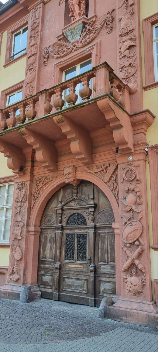Ein altes Gebäude in Heidelberg, Deutschland, mit einer hölzernen Tür, Fenstern und detaillierten Verzierungen an seiner Fassade.