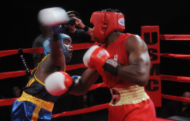 Zwei Boxer im Ring mit einem Fotografen und Zuschauern im Hintergrund bei dramatischer Beleuchtung.