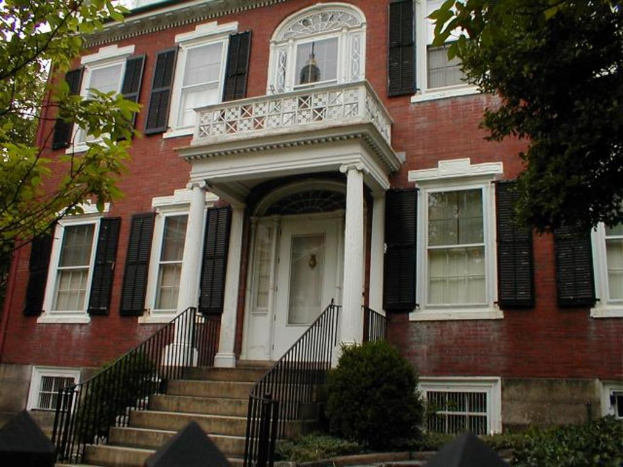 Ein Gebäude mit Glasfenstern und weißen Rändern, das eine Treppe mit schwarzen Gittern auf beiden Seiten und von Bäumen flankiert ist.