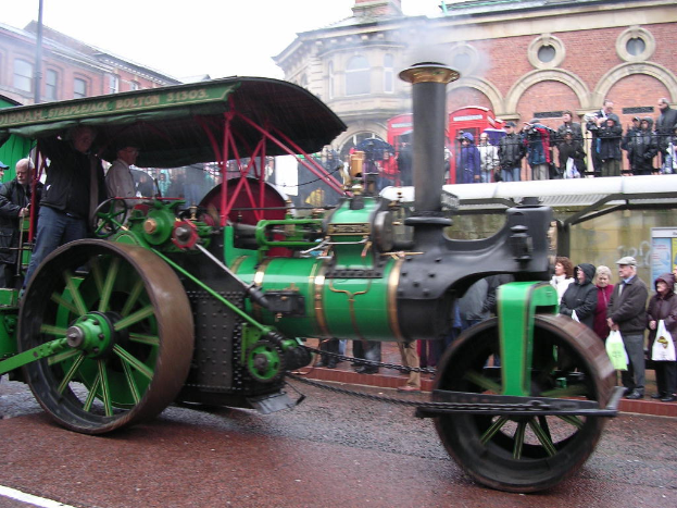 Ein Motor ist mittig positioniert mit Gebäuden oben und Menschen auf der rechten Seite des Bildes.