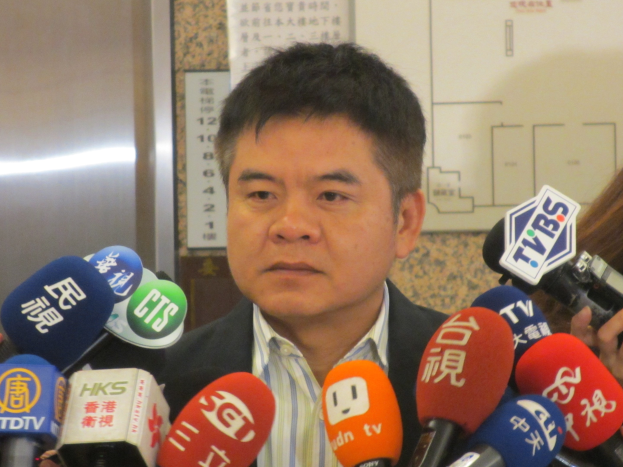 Ein Mann im Anzug und Krawatte spricht zu Reportern mit einer Frau, die rechts eine Kamera hält.