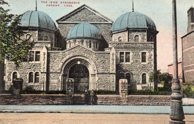 Alte Ansichtskarte der jüdischen Synagoge in Cardiff, Ontario, Kanada, die ein Gebäude mit Fenstern, Türen und Bögen zeigt, umgeben von Pflanzen, einem Zaun, Bäumen, einem Pfahl und einem bewölkten Himmel, mit Text oben.