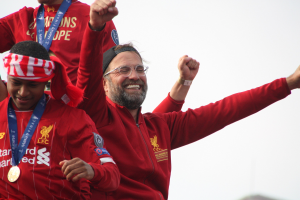 Liverpool-Trainer Jürgen Klopp feiert mit Spielern und Stab nach dem Gewinn der UEFA Champions League, trägt eine rote Jacke und hat zwei Medaillengewinner neben sich unter einem sichtbaren Himmel.