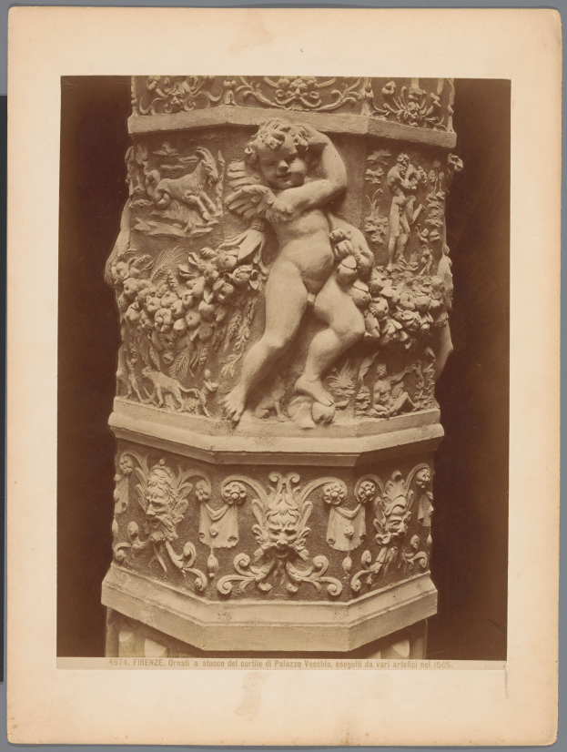 Eine schwarze und weiße Statue eines Cherubs auf einem kunstvoll verzierten Sockel, mit dem Cherub in einer anmutigen Pose, Arme ausgestreckt, Kopf geneigt und Augen geschlossen.