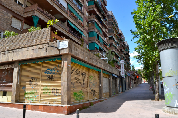 Eine Szene mit Gebäuden, die Fenster, grünen Kältern, Geschäften, Schildern und umgebenden Bäumen und Pflanzen zeigen.