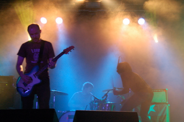 Ein musikalisches Konzert mit Scheinwerfern oben, Musikern, die Instrumente spielen, in der Mitte und Lautsprechern auf der linken und rechten Seite.