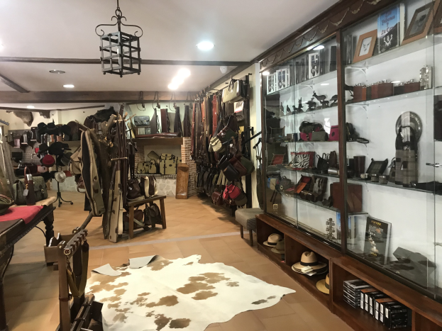 Ein vollgestelltes Boutique-Zimmer in Barcelona mit einem Kuhfellteppich, hängenden Kleidern, Hüten, Fotorahmen und verschiedenen Gegenständen in Schränken, beleuchtet von Deckenlampen und einem Kronleuchter.