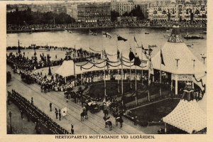 Schwarz-weiß-Foto einer Menschenmenge bei einem Karneval mit Zelten, Fahnen, Stangen, Pferden, Gebäuden, Bäumen und Wasser im Hintergrund, mit Text unten.