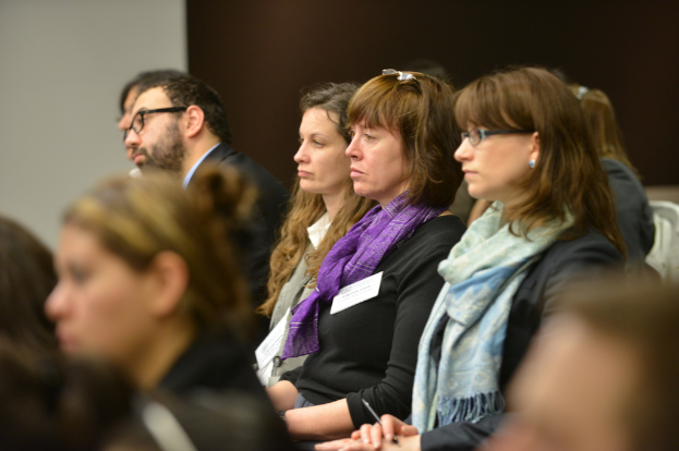 Frauen sitzen in Stühlen in der Mitte des Bildes, mit einer Person im Anzug im Hintergrund.