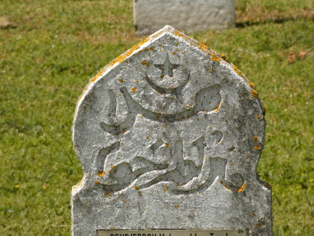 Grabstein mit arabischer Inschrift in einem grasbewachsenen Friedhof.