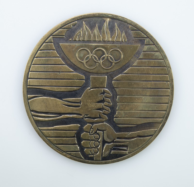 Eine runde Bronzemedaille mit goldenem Schimmer, die das Olympische Logo in der Mitte zeigt, vor einem weißen Hintergrund.