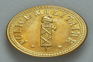 Eine Goldm├╝nze mit der Aufschrift "Police Militaire" auf einem wei├čem Hintergrund.