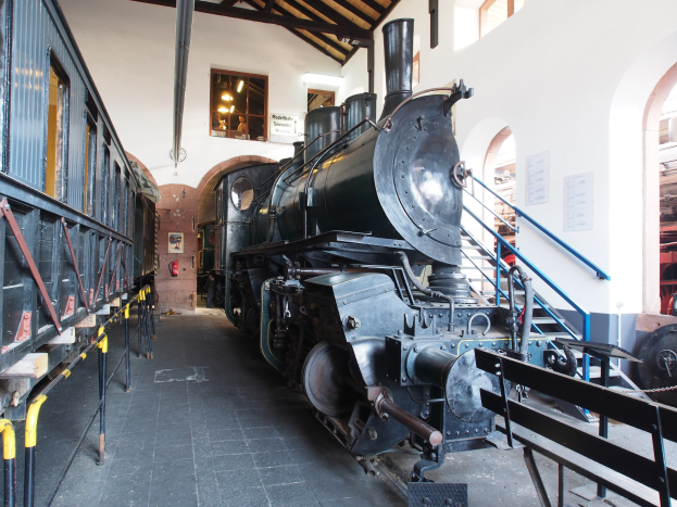 Alte Dampflokomotive in Museumsgebäude mit Informationsschildern, Geländern und Beleuchtung.