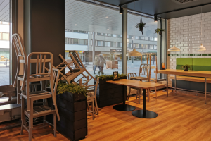 Ein Restaurant in Berlin, Deutschland, mit Holztischen und -stühlen vor einem großen Fenster, das Menschen auf der Straße, Gebäude und den Himmel zeigt.