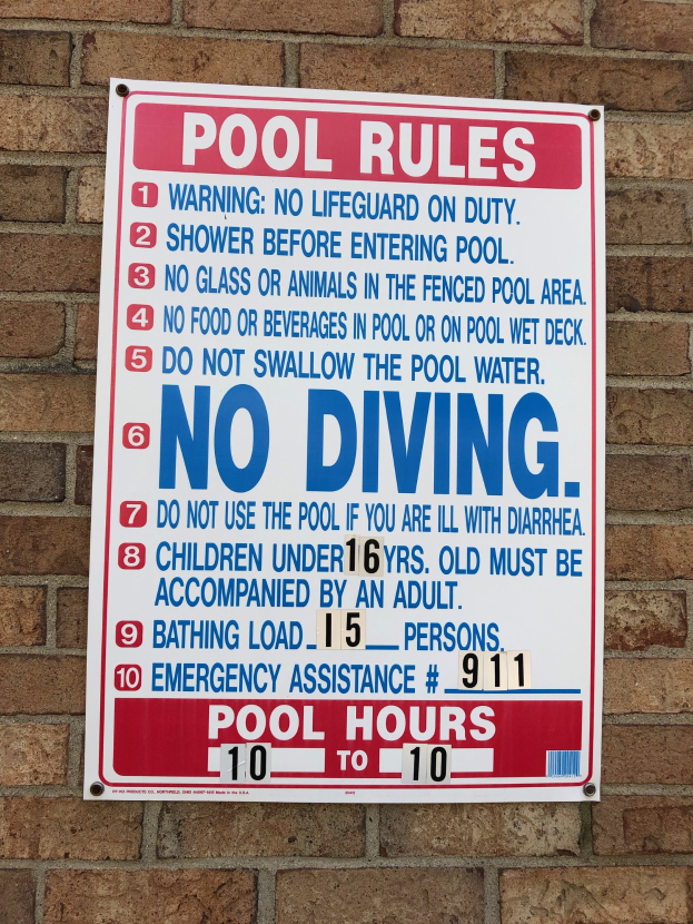Weißer Schild mit schwarzer Schrift, auf dem "Pool Rules: No Diving" steht, an der Seite eines Backsteingebäudes angebracht