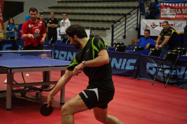 Eine Gruppe von Menschen in verschiedenen Farben, darunter schwarz, weiß und blau, sitzt um einen Tisch mit einem Spiel in einem Fortschritt, mit Stühlen und einer Treppe im Hintergrund.