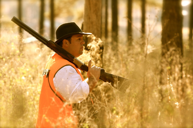 Eine Person hält eine Waffe mit Pflanzen vor sich und Bäumen im Hintergrund.