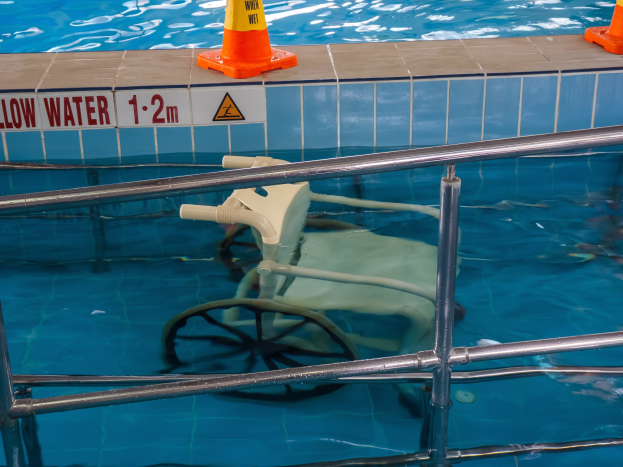 Schwimmbecken mit einem Stuhl in der Mitte, umgeben von Sicherheitskegeln und einem Geländer und einer Wandtafel mit Text.
