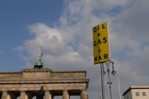 Das Brandenburger Tor in Berlin, Deutschland, mit einem gelben Schild, auf dem "Öl- und Gaskrieg" steht, im Vordergrund, Gebäuden, Polen, Lichtern, einer Statue und einem bewölkten Himmel im Hintergrund.