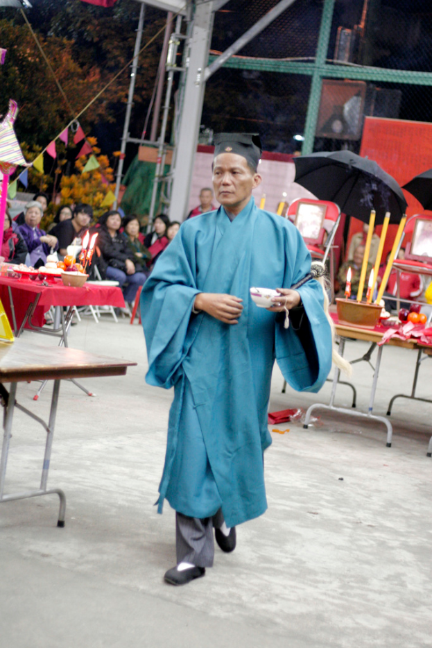 Eine Szene mit Bäumen, ein paar Menschen, einem Schirm und einem Tisch mit einer Kerze, Schüssel und Tellern.
