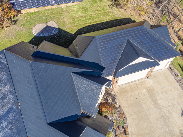 Ein Haus mit Solarpanelen auf dem Dach, umgeben von Bäumen, Gras und einem Zaun, aus der Vogelperspektive betrachtet.