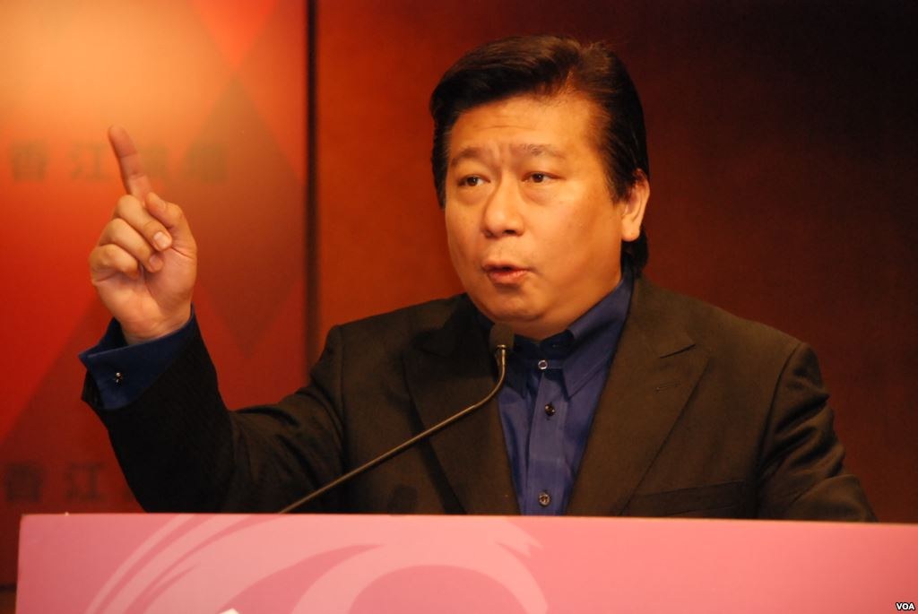 Ein Mann im Anzug und Krawatte, der vor einem Rednerpult mit Mikrofon spricht und ernst wirkt.