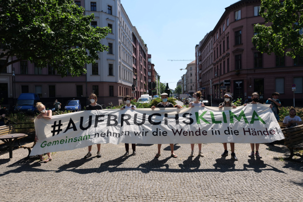 Eine Gruppe von Menschen mit Masken, die ein Banner mit der Aufschrift 'Aufbruchsklima' halten, während sie an einer Klimaprotest in Berlin, Deutschland teilnehmen.