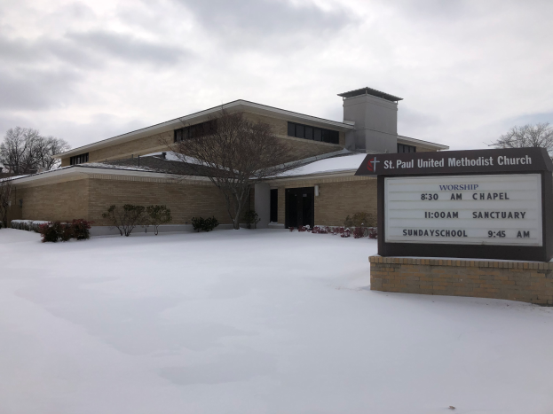 St. Paul United Methodist Church, ein Gebäude mit Fenstern und Türen, umgeben von Pflanzen und Bäumen, mit Schnee auf dem Boden und einem bewölkten Himmel im Hintergrund; ein Schild mit Text ist auf der rechten Seite des Bildes sichtbar.