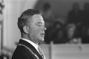 Ein Mann im Anzug und Krawatte steht an einem Rednerpult mit einem Mikrofon und spricht zu einer unscharfen Menge, der ein Politiker zu sein scheint.