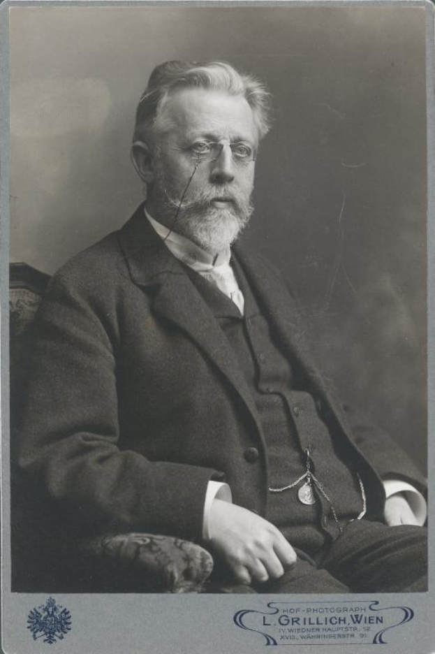 Ein Schwarz-Weiß-Foto eines bärtigen, Brillenschlangen-Mannes, der in einem Stuhl sitzt, mit dem Text "L. Grillich Wien, der Gründer der deutschen Revolution" unten.