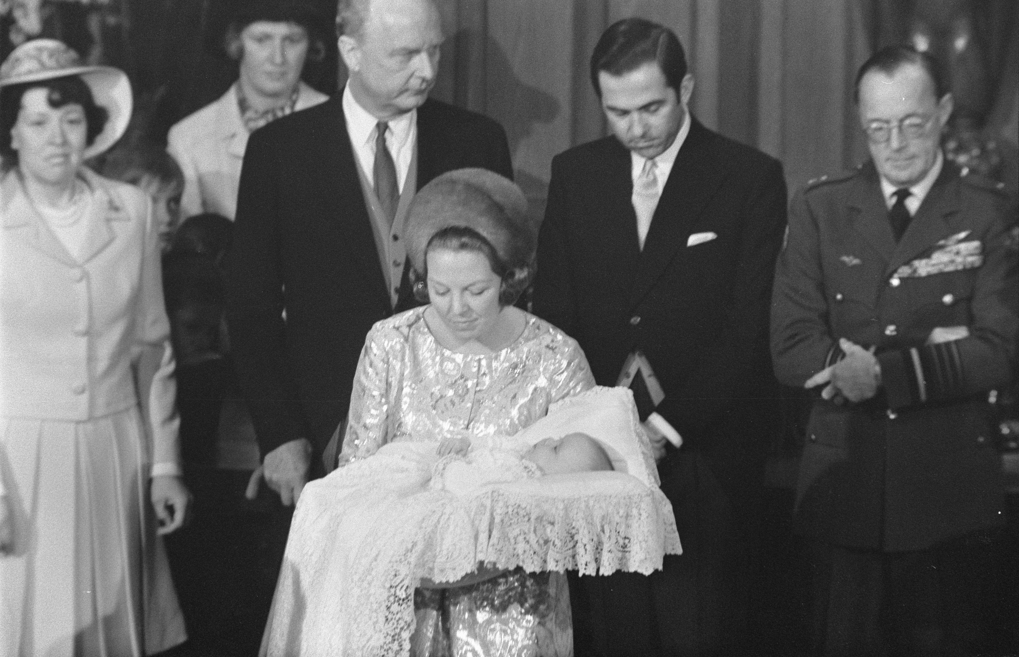 Königin Elizabeth II. wiegt ihren neugeborenen Prinz Philip in den Armen, während Prinz Philip, Herzog von Edinburgh, neben ihr in einem Anzug und Krawatte steht, mit Vorhängen im Hintergrund.