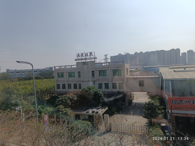 Eine Stadtansicht von einem Gebäude aus, mit verschiedenen Gebäuden, Bäumen, Straßenlaternen, Strommasten, Fahrzeugen und einer Fabrik mit einem Schild "Zhejiang Zhongshan Automotive Machinery Co., Ltd." unter einem klaren blauen Himmel.