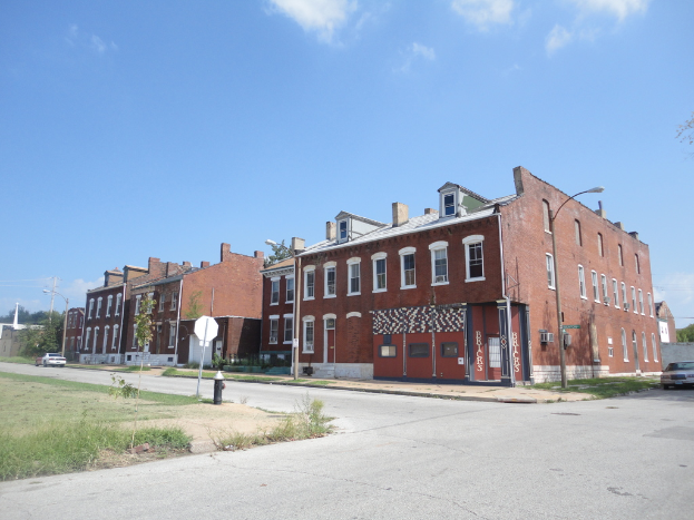 Ein Gebäude mit Straßenlaternen, Pfählen und Bäumen, mit Fahrzeugen auf beiden Seiten, einem Gehweg und Gras unten und einem Himmel oben.