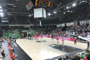 Basketballspiel in einer gro├čen Arena mit Zuschauern, mit einem Scoreboard, das "Asvel vs Galatasaray" anzeigt.