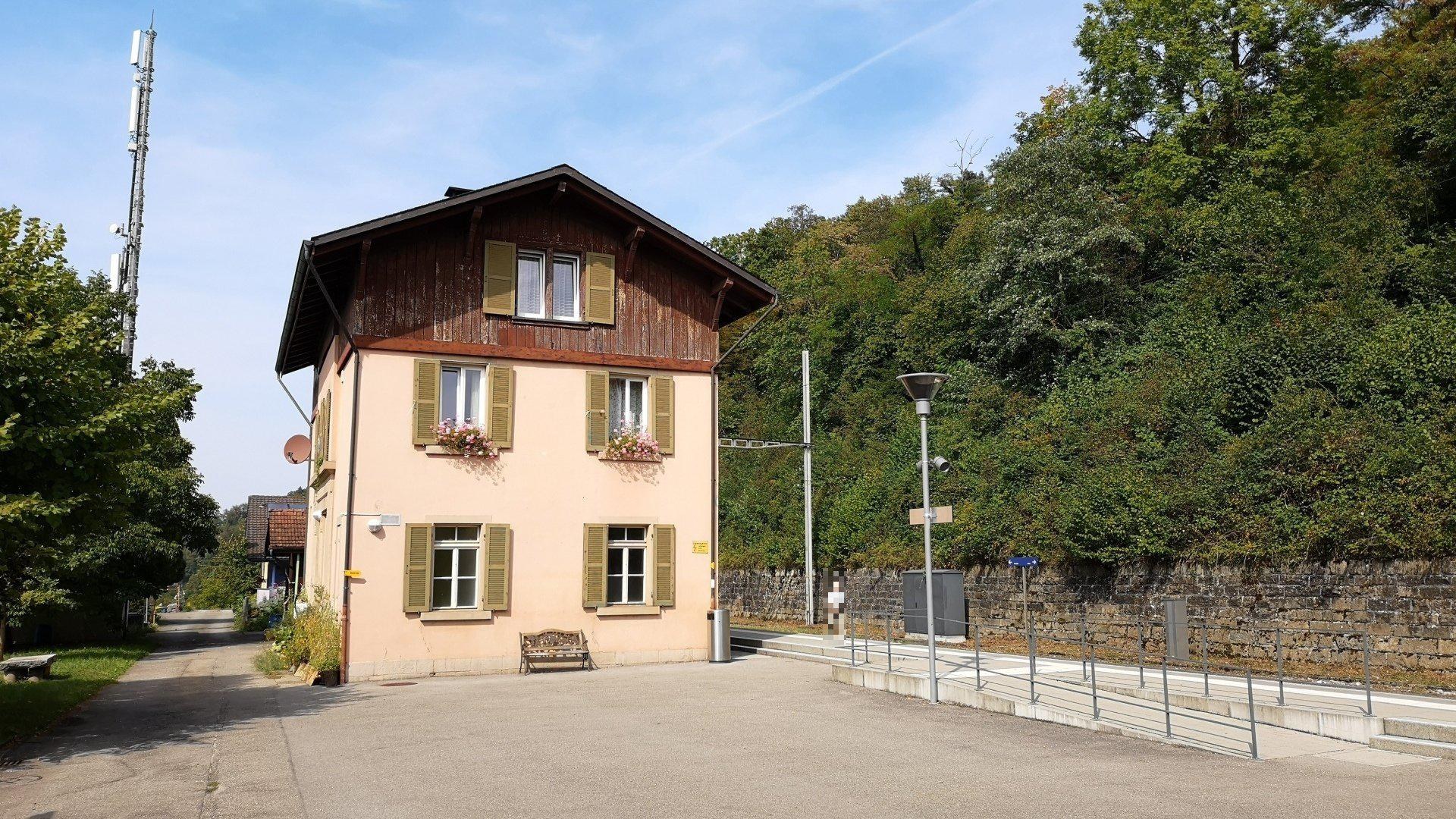 Ferienhaus in Baden-Württemberg, Deutschland zum Verkauf, mit einem Gebäude mit zahlreichen Fenstern, einer vorderen Einfriedung und umgebenden Straßen-Elementen, Pflanzen und Bäumen unter einem bewölkten Himmel.