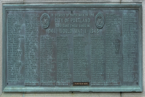 Metallplatte an einer Gebäudewand angebracht mit der Aufschrift "Denkmal für die Stadt Portland" in fetter schwarzer Schrift, eingerahmt von einem dekorativen Rand.