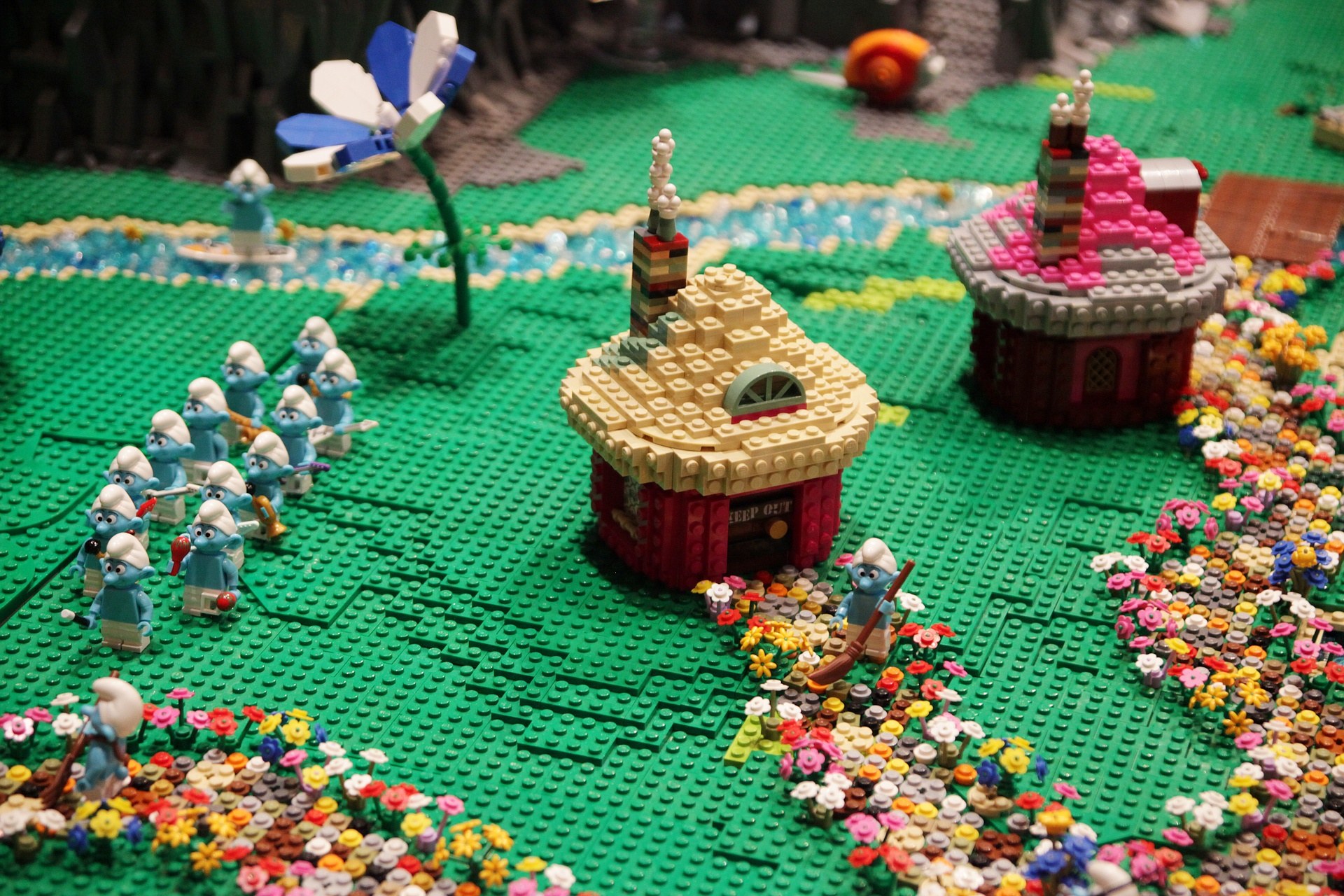 Ein Lego-Modell einer Kleinstadt mit verschiedenen Blumen, Spielzeugen, Häusern, Pflanzen und anderen Gegenständen vor einem leicht unscharfen Hintergrund.