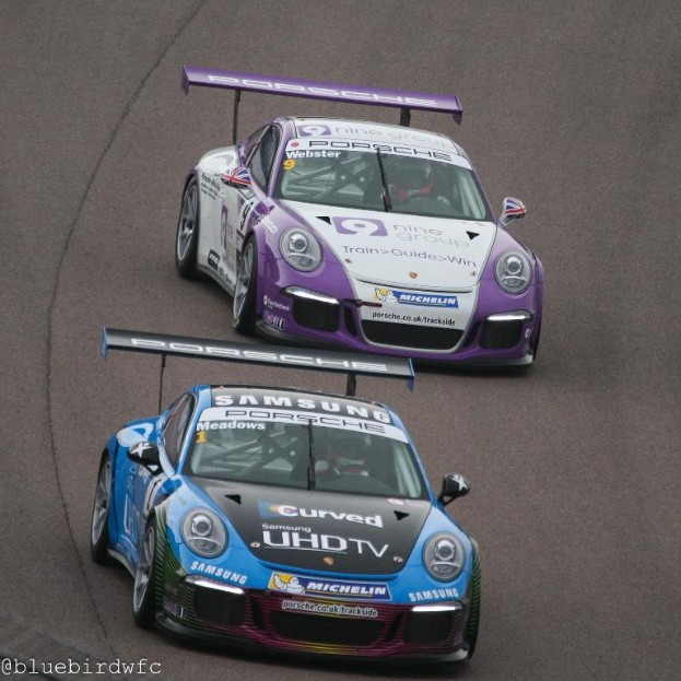 Zwei Autos fahren auf einer Straße außerhalb der Stadt mit Text in der unteren linken Ecke.