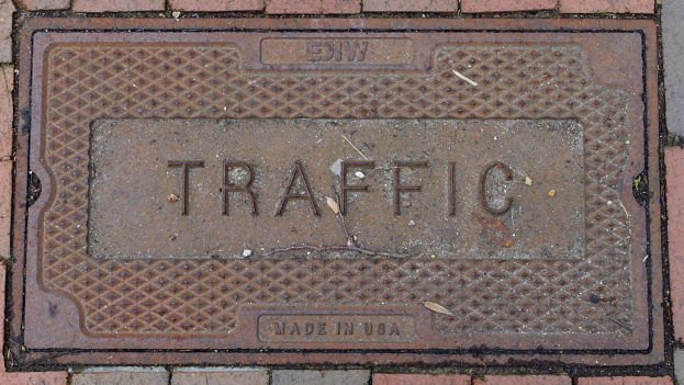 Ein Ziegelsteinweg mit einer Metallgullideckel, auf der das Wort "Verkehr" steht.