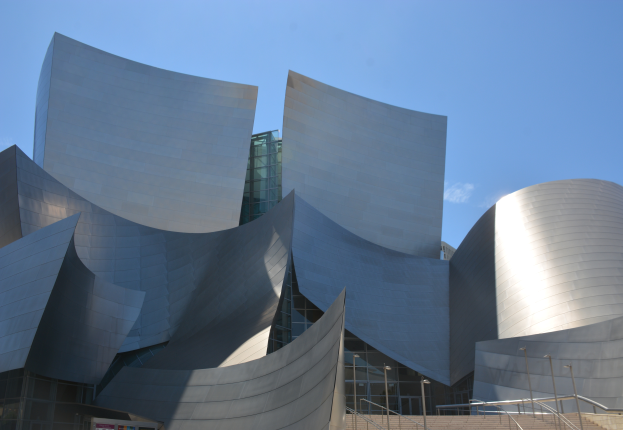Das Künstlerkonzertgebäude in Los Angeles, ein modernes Gebäude mit Glaswänden und Treppen mit Geländern, die zum Eingang führen, umgeben von Laternenmasten, mit einer Tafel mit Text im Vordergrund und einem bewölkten Himmel im Hintergrund.