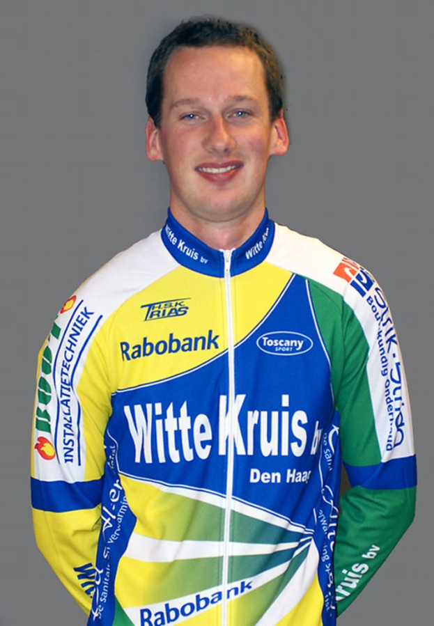 Ein männlicher Athlet posiert für ein Foto, trägt ein Hemd mit mehreren Sponsoren-Logos.