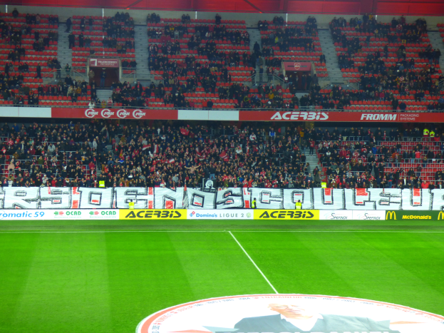 Ein Fußballfeld mit einer großen Zuschauermenge auf den Tribünen, umgeben von Texttafeln und einem Logo mit Text unten.