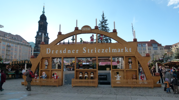 Ein lebendiger Weihnachtsmarkt in Dresden, Deutschland, mit Menschen, die herumlaufen, einem Bogen mit Text, Tälern, Gebäuden mit Fenstern und einem bewölktem Himmel.