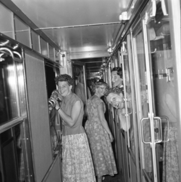 Eine Gruppe von Frauen steht auf einem schwarzen und weißen Zug mit Türen auf beiden Seiten und Lichtern öben.