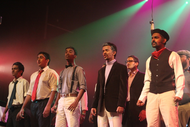 Eine Gruppe von Männern spielt ein Drama auf der Bühne mit grünen Spotlights im Hintergrund.