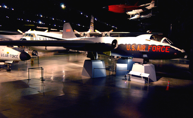 Eine Gruppe von Kampfflugzeugen in einem dunklen Museumsraum, umgeben von St├Ąnden, Verkehrskegeln und anderen Bodenobjekten.