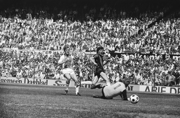 Schwarzes Foto von Fußballspielern im Einsatz auf einem Feld mit Zuschauern im Hintergrund und einem "Bundesliga 1978-79 Ajax 1-1 Hannover 96"-Banner.