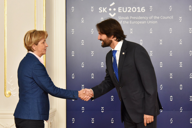Bundeskanzlerin Angela Merkel und Bundespräsident Joachim Gauck schütteln sich die Hände vor einer Wand mit einem 'EU-Gipfel'-Schild und einer Tür im Hintergrund, beide lächeln.