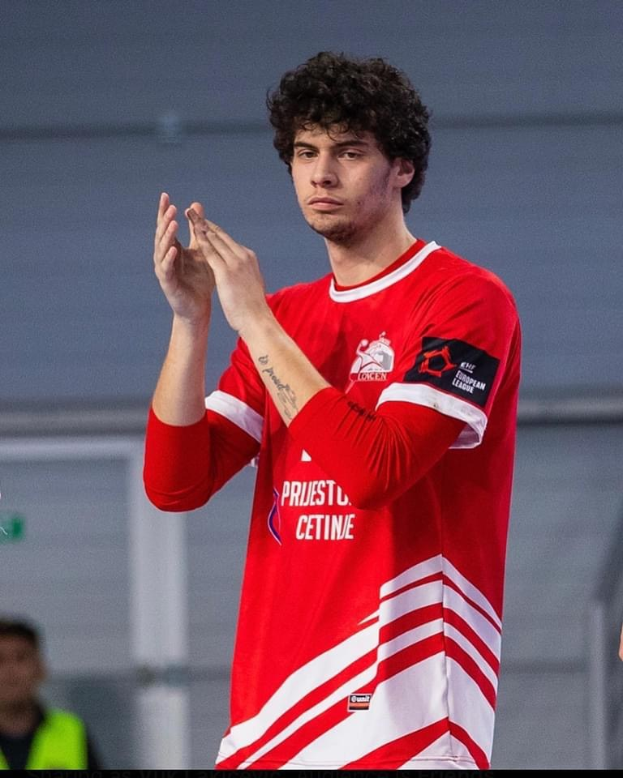 Ein Mann in einem roten und weißen Hemd klatscht in den Händen im Vordergrund, mit einer anderen Person und einer Wand im Hintergrund, und Text, der unten 'Kopenhagen Futsal Club - Foto 1' liest.